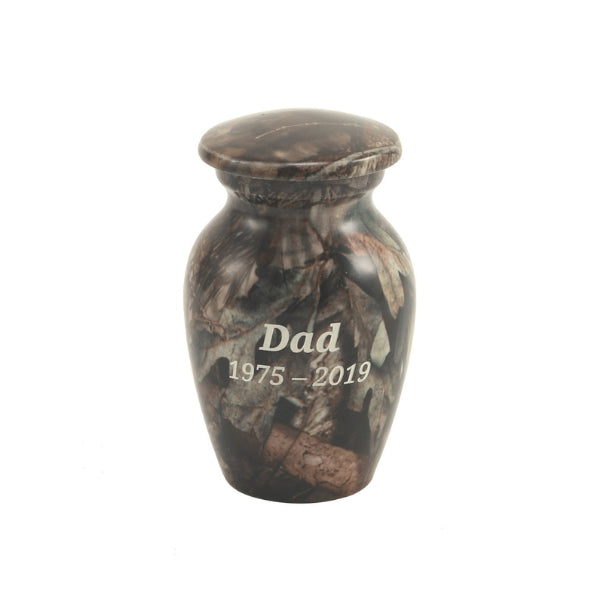 The Mossy Oak Camo Keepsake Urn, available at Magnolia Cremations, is a small aluminum urn featuring a detailed camouflage pattern, ideal for honoring a loved one with a passion for nature and the outdoors. The urn has a rounded shape with a matching lid and includes an engraved inscription, showcasing the option for personalization. Designed to hold a small portion of ashes, this keepsake allows family members to share in remembrance.