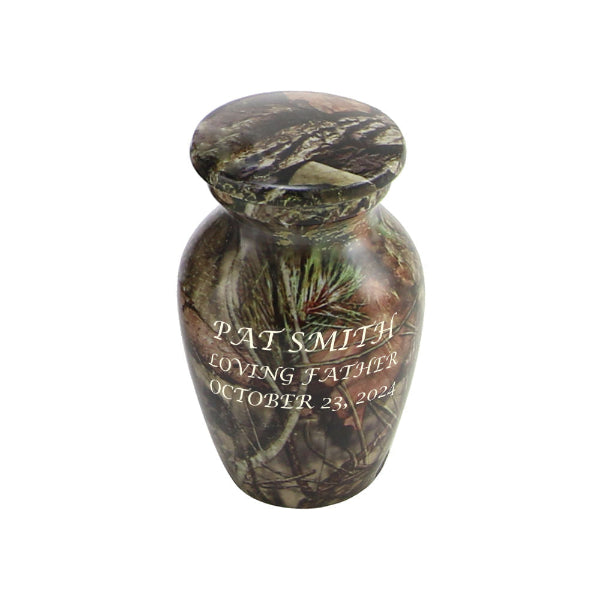The Mossy Oak Camo Keepsake Urn, available at Magnolia Cremations, is a small aluminum urn featuring a lifelike camouflage pattern, perfect for commemorating a loved one who cherished the outdoors. The urn has a smooth, rounded shape with a matching lid and includes an engraved inscription, demonstrating the option for personalization. Designed to hold a small portion of ashes, this keepsake allows multiple family members to share in honoring their loved one’s memory.