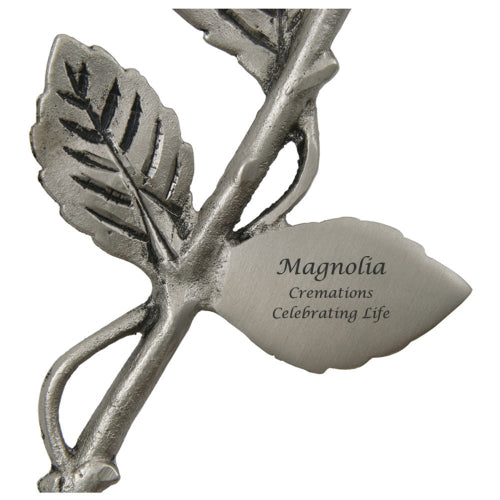 A close-up view of the Pewter Rose Keepsake from Magnolia Cremations, showcasing its intricately designed stem and leaves with a brushed silver finish. A metal leaf-shaped plaque is attached, offering space for a personalized engraving. This elegant memorial piece is crafted to hold a small portion of ashes, serving as a lasting tribute.