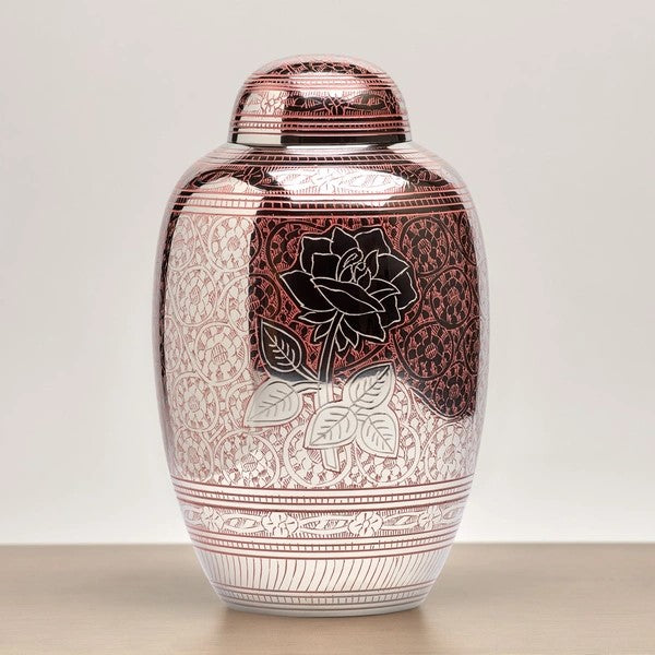 A close-up of the Traditional Rose Memorial Urn, available at Magnolia Cremations. This full-size brass urn features a reflective pink and silver finish with an intricate floral engraving and a bold silver rose design at its center, symbolizing love and remembrance.