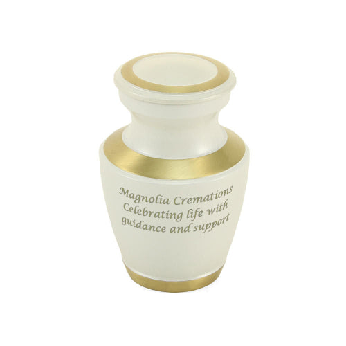 The Trinity Pearl Keepsake Urn, available at Magnolia Cremations, is a small, elegant urn with a high-gloss creamy white finish and gold-tone accents on the lid, rim, and base. Crafted from brass, this keepsake urn offers a refined and contemporary tribute. The urn is engraved with a message, showcasing the option for personalization. Designed to hold a small portion of ashes, it allows multiple family members to share in remembrance.