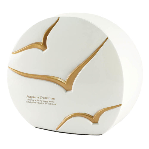 The Windham Going Home Glossy White Memorial Urn, available at Magnolia Cremations, features a unique circular shape with a high-gloss white finish. Three gracefully sculpted gold birds in flight add depth and symbolism, representing a peaceful journey. The urn’s modern design blends elegance with artistry, making it a refined tribute to a loved one. Engraving is shown as an available option.